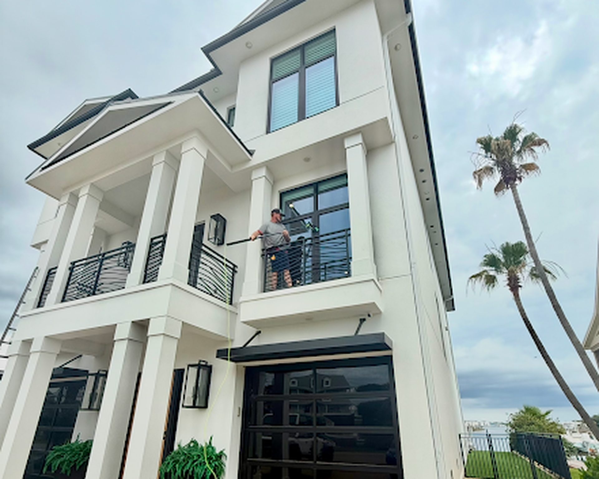 Window cleaner on a balcony using a water-fed pole at a Gulf Shores home
